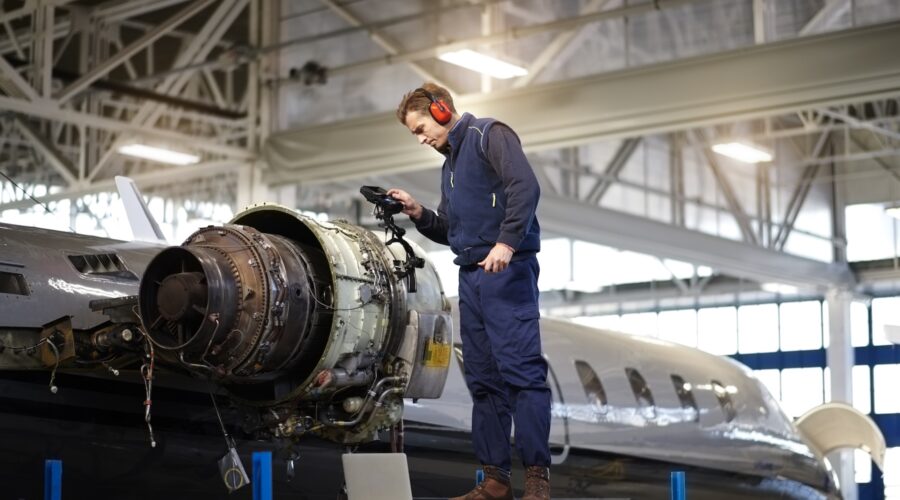 Aircraft engineer in the hangar repairing and maintaining airplane jet engine.